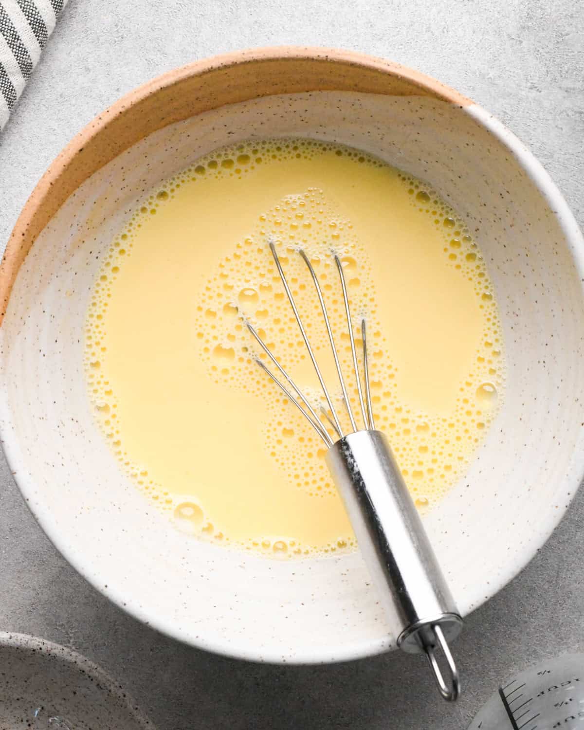 Making rice pudding: overhead photo of egg and milk mixture being whisked together in a white speckled bowl.