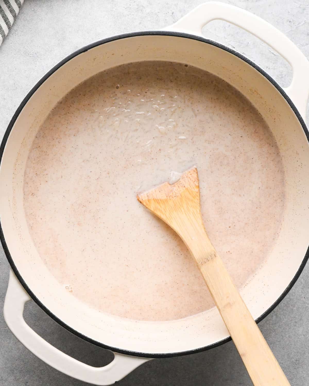 Making rice pudding: overhead photo of wet and dry ingredients for rice pudding stirred together with a wooden spoon and simmering in a large white pot.