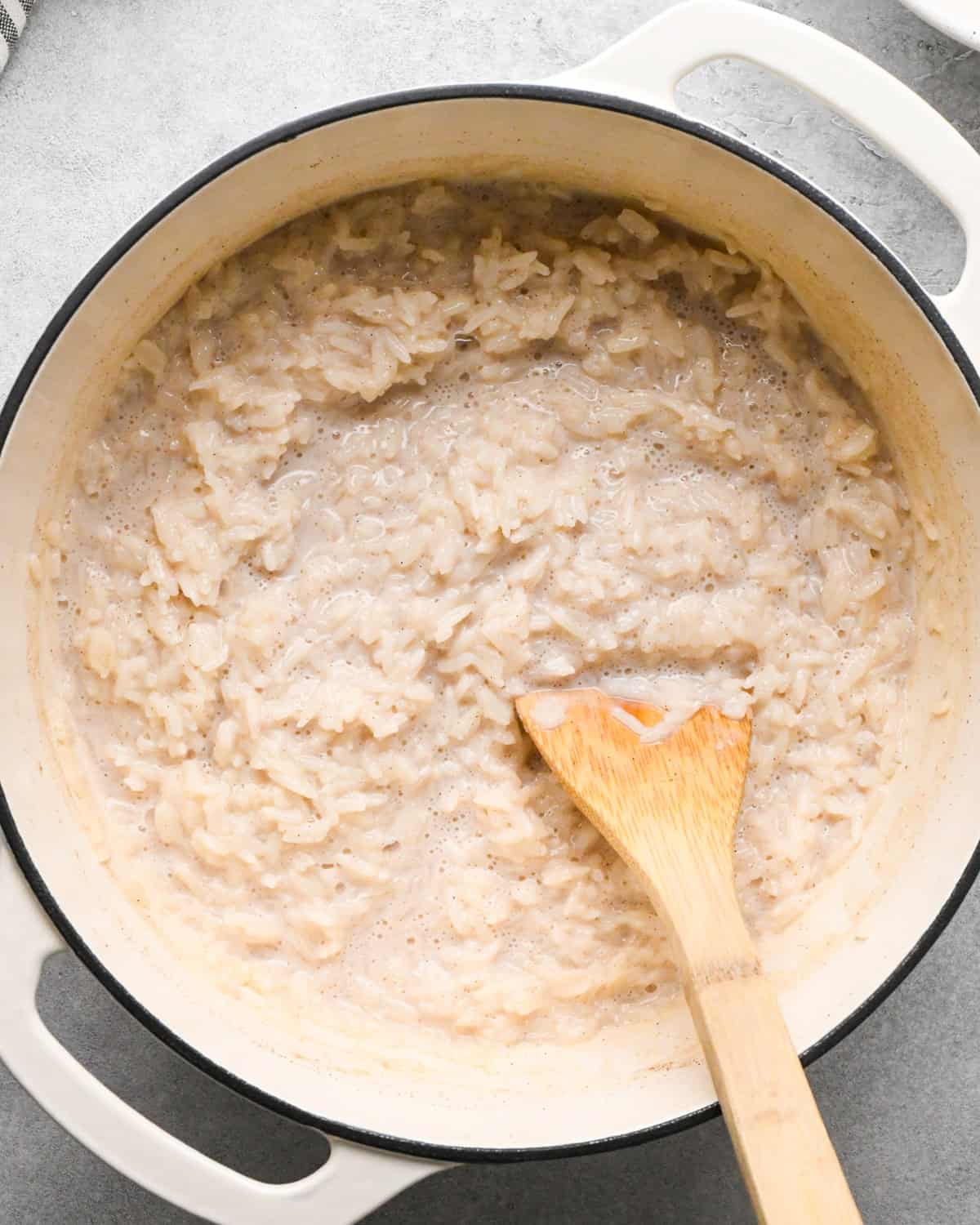 Making rice pudding: overhead photo of cooked rice mixture in a large pot with a wooden spoon sitting in the pot.