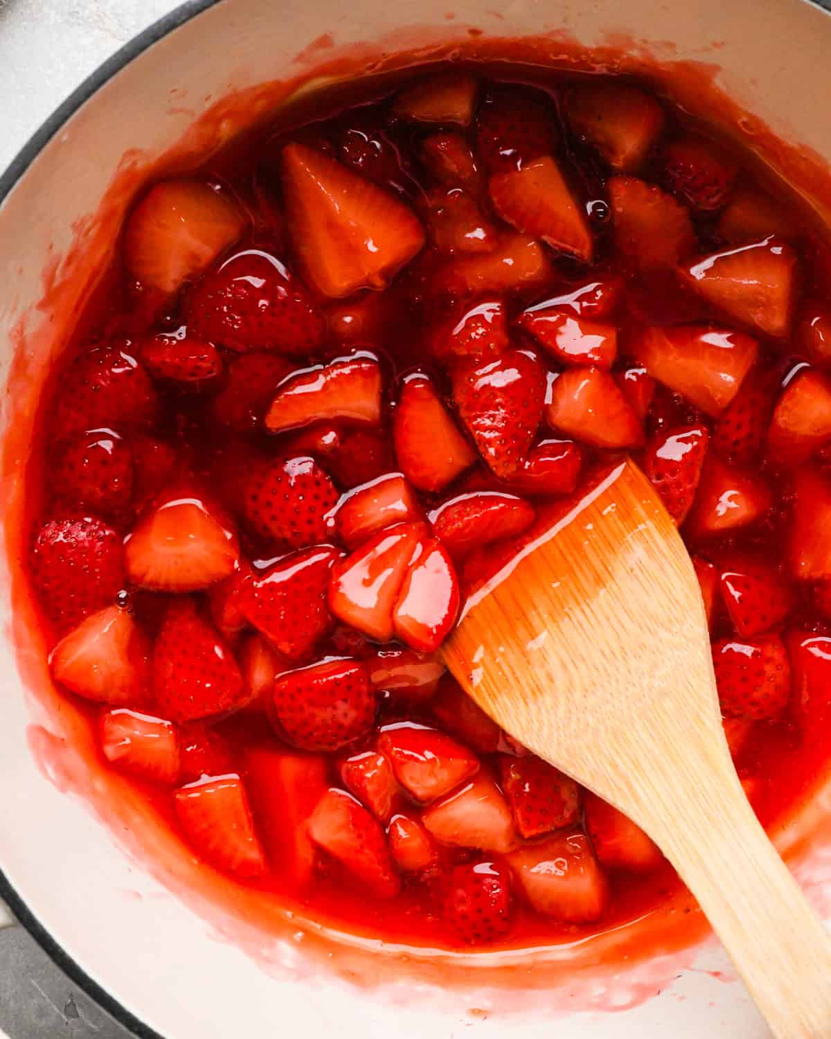 Making homemade strawberry sauce: overhead photo of completed strawberry sauce being stirred with a wooden spoon.