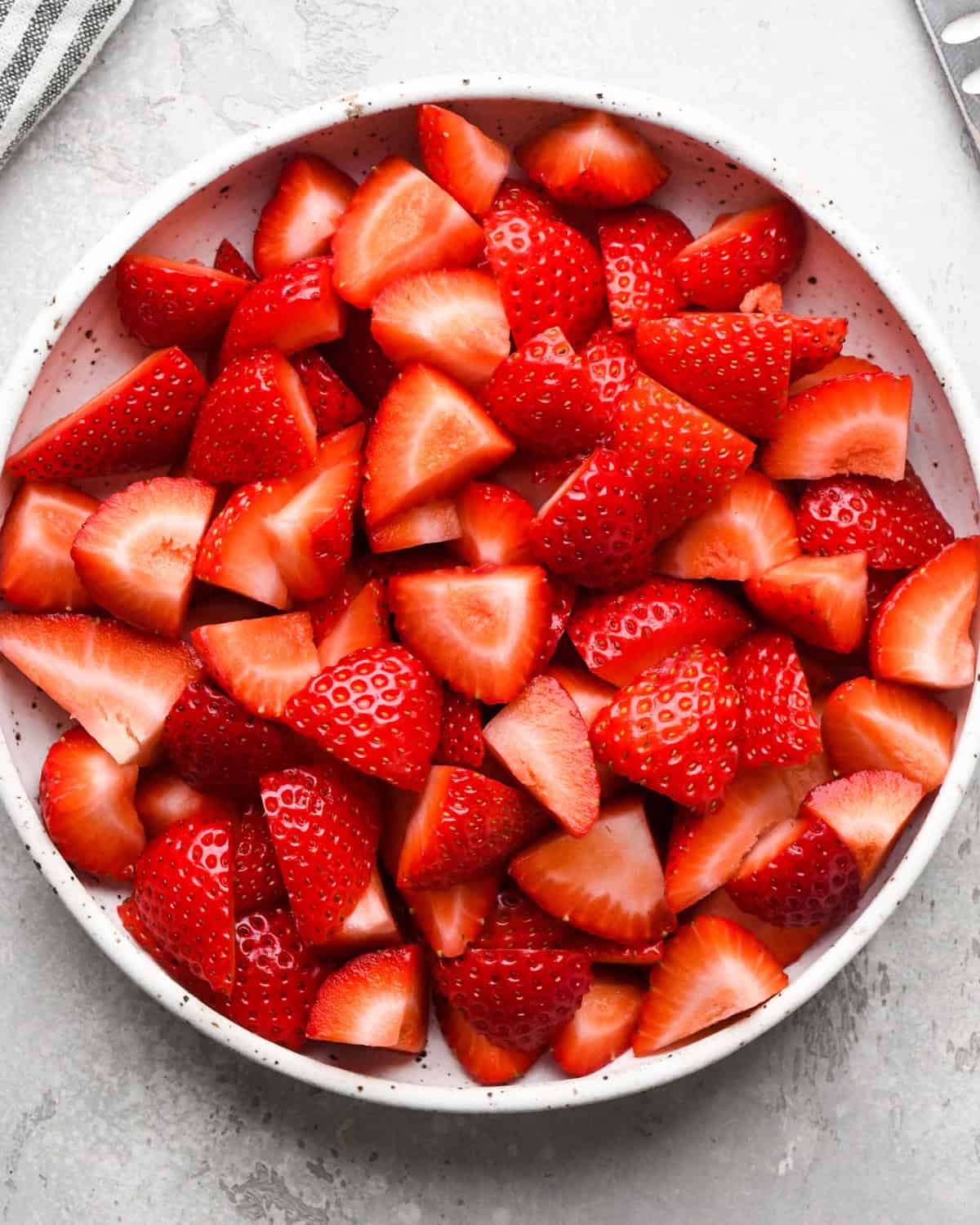 Making homemade strawberry sauce: overhead photo of a white speckled bowl filled with fresh sliced strawberries.