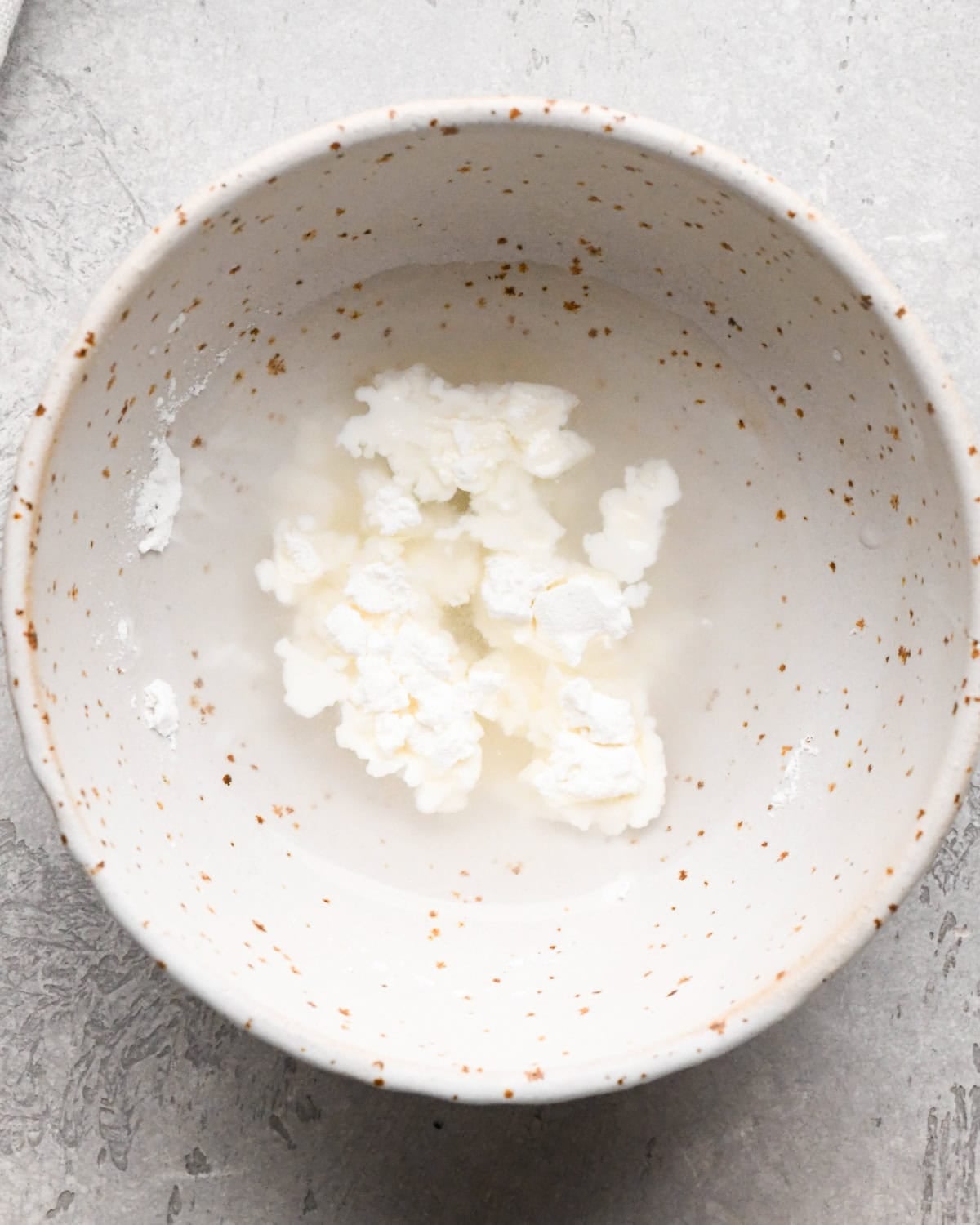 Making homemade strawberry sauce: overhead photo of water and cornstarch in a white speckled bowl.