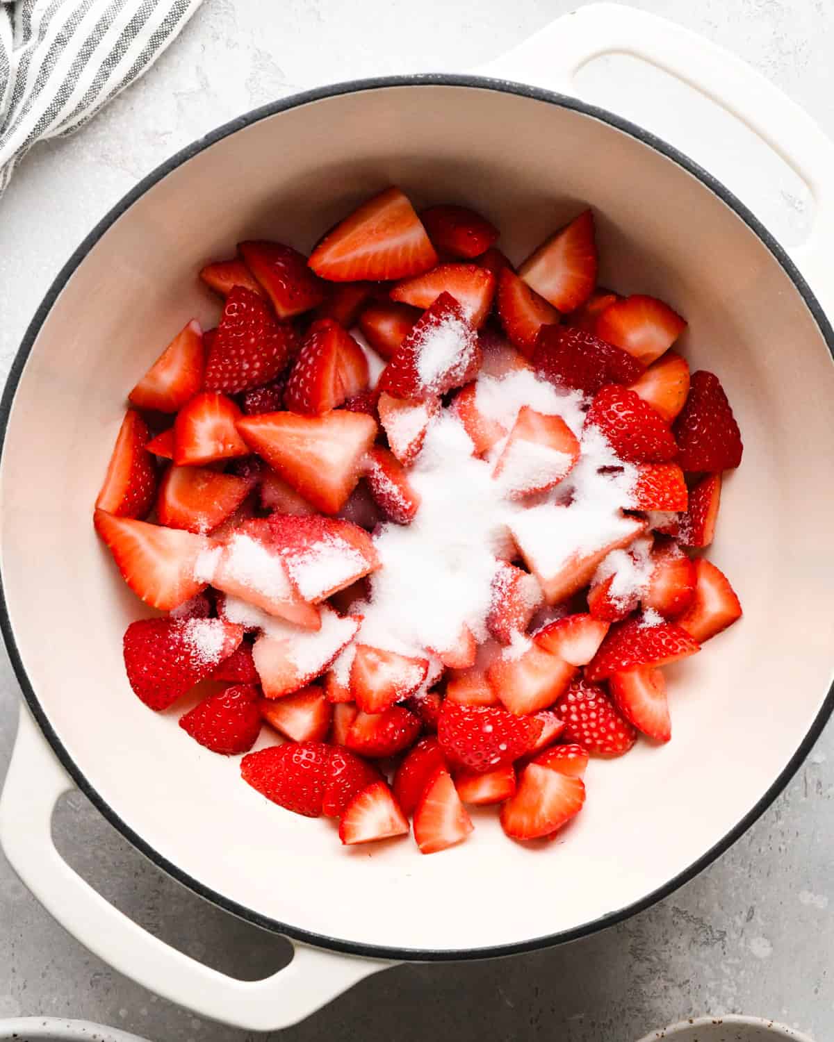 Making homemade strawberry sauce: overhead photo of strawberries, sugar, lemon juice, and cornstarch/water mixture in a large white pot.