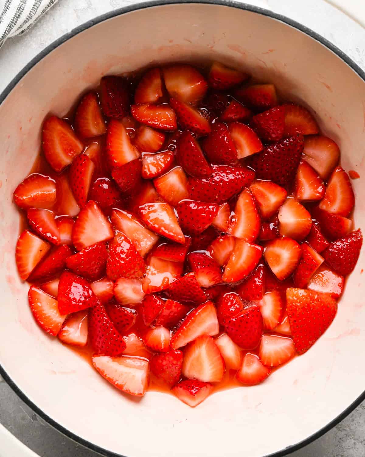 Making homemade strawberry sauce: overhead photo of strawberries, sugar, lemon juice, and cornstarch/water mixture simmering together in a large white pot.