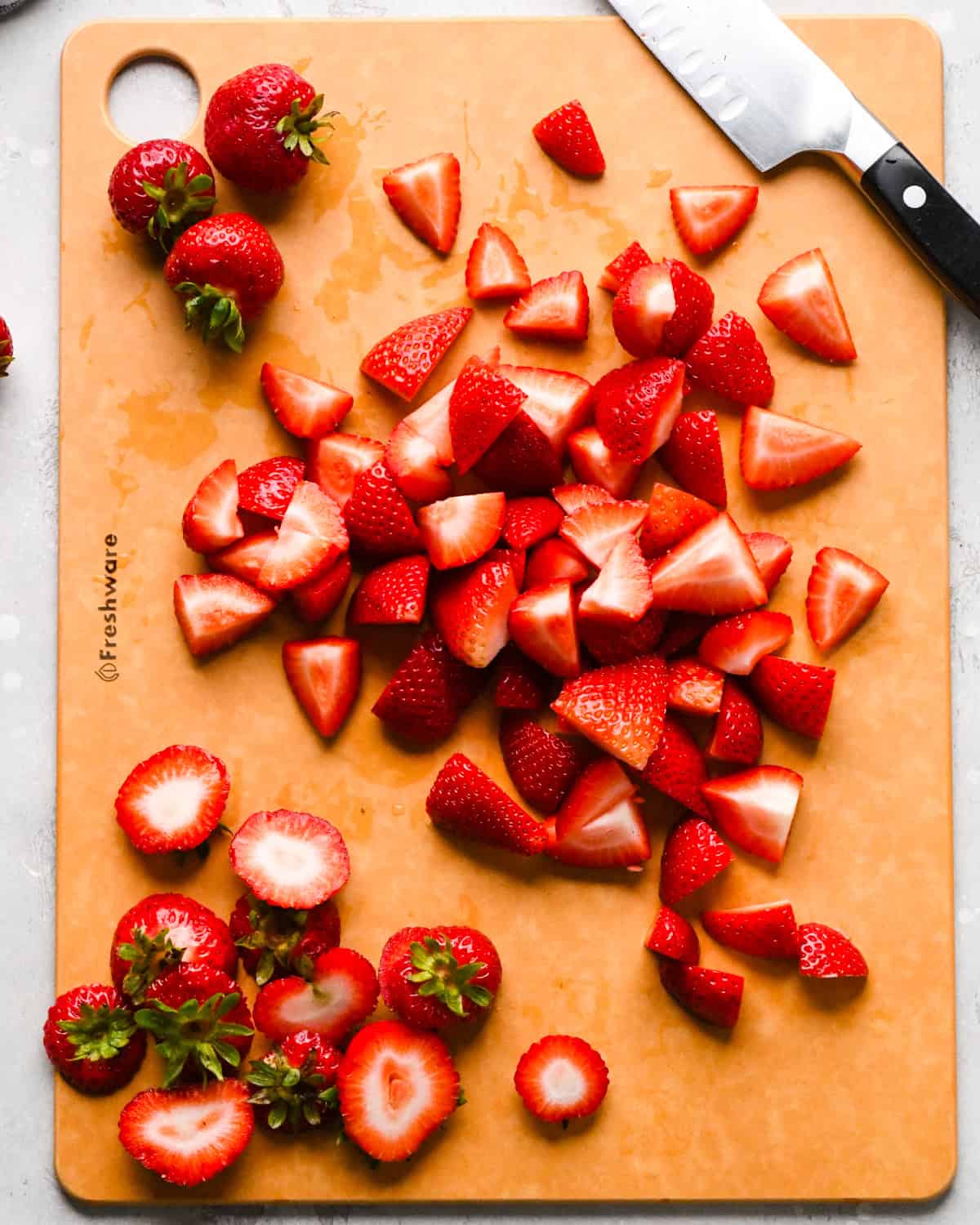 Making homemade strawberry sauce: overhead photo of sliced fresh strawberries on top of a brown cutting board with a knife sitting on top of the board.