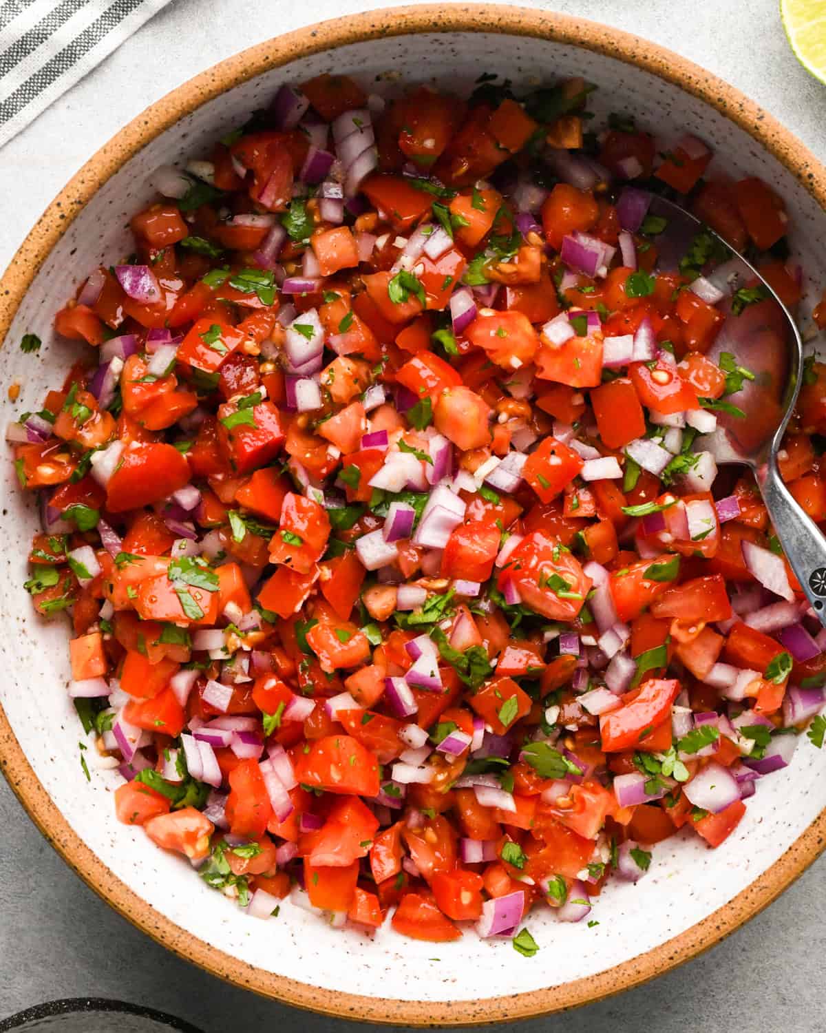 Making pico de Gallo: overhead photo of all ingredients mixed together with a spoon in a large white bowl.