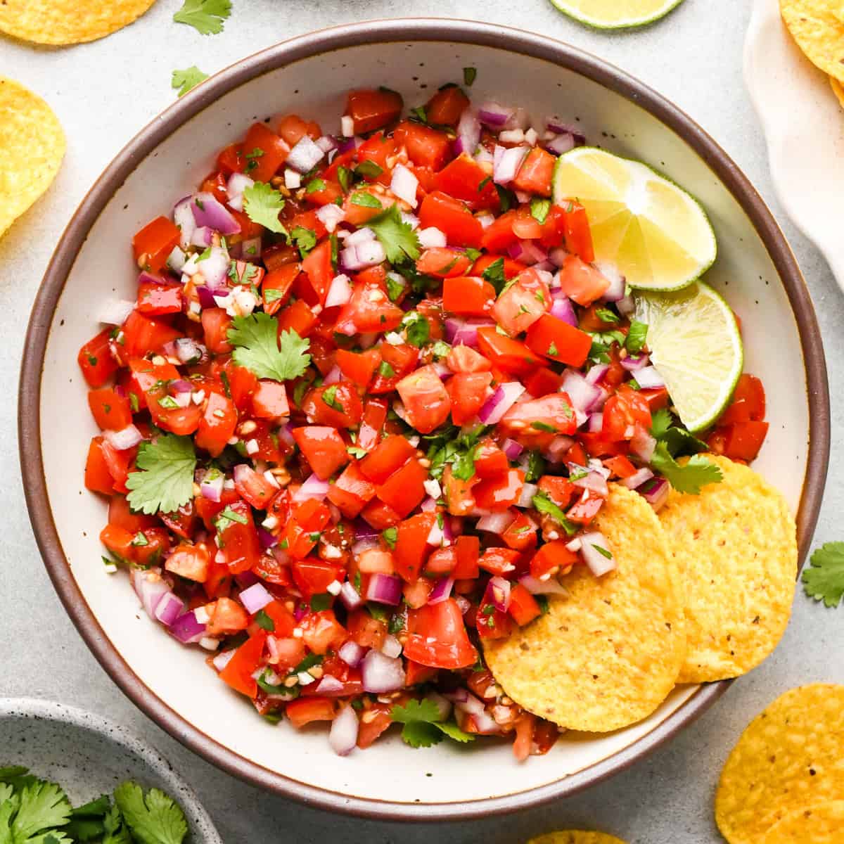 Bowl of homemade pico de gallo made with diced tomatoes, red onion, cilantro, and lime, served with tortilla chips on the side.