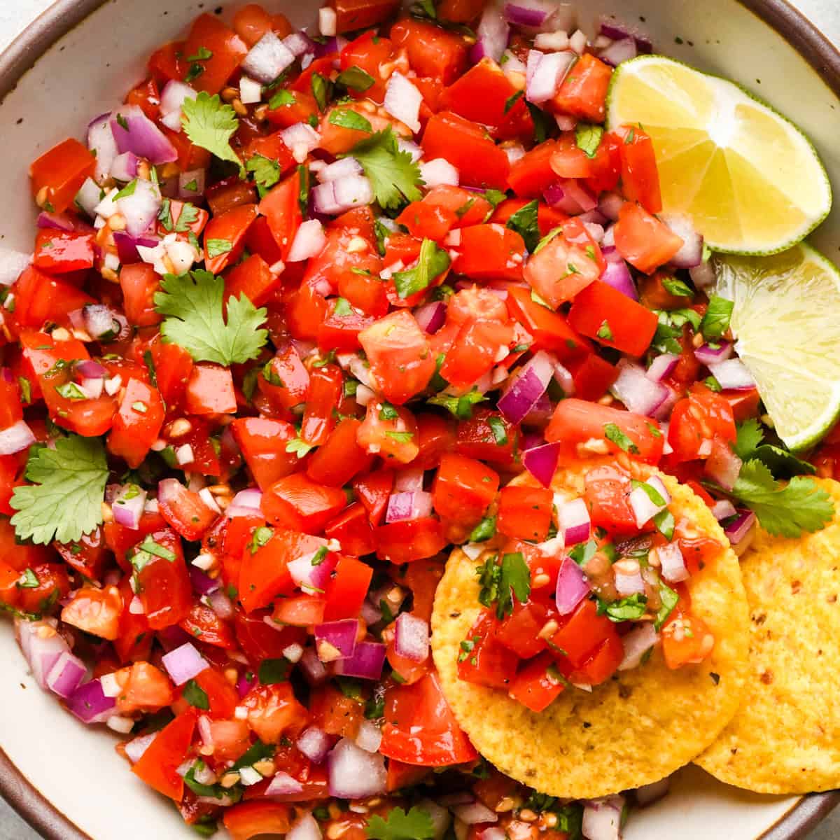 Bowl of homemade pico de gallo made with diced tomatoes, red onion, cilantro, and lime, served with tortilla chips on the side.
