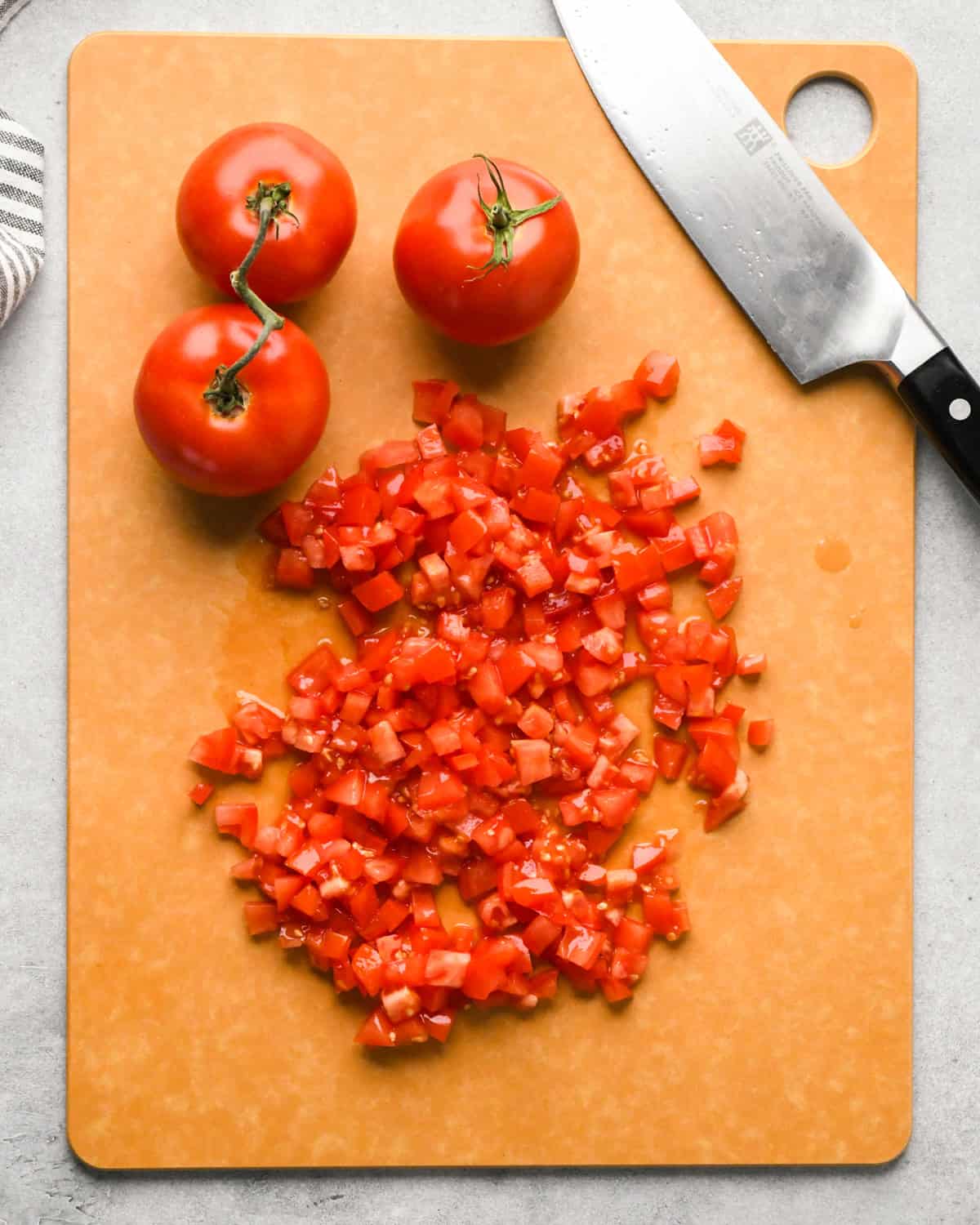 Making pico de Gallo: overhead photo of diced tomatoes sitting on a brown cutting board with a knife resting on the board.