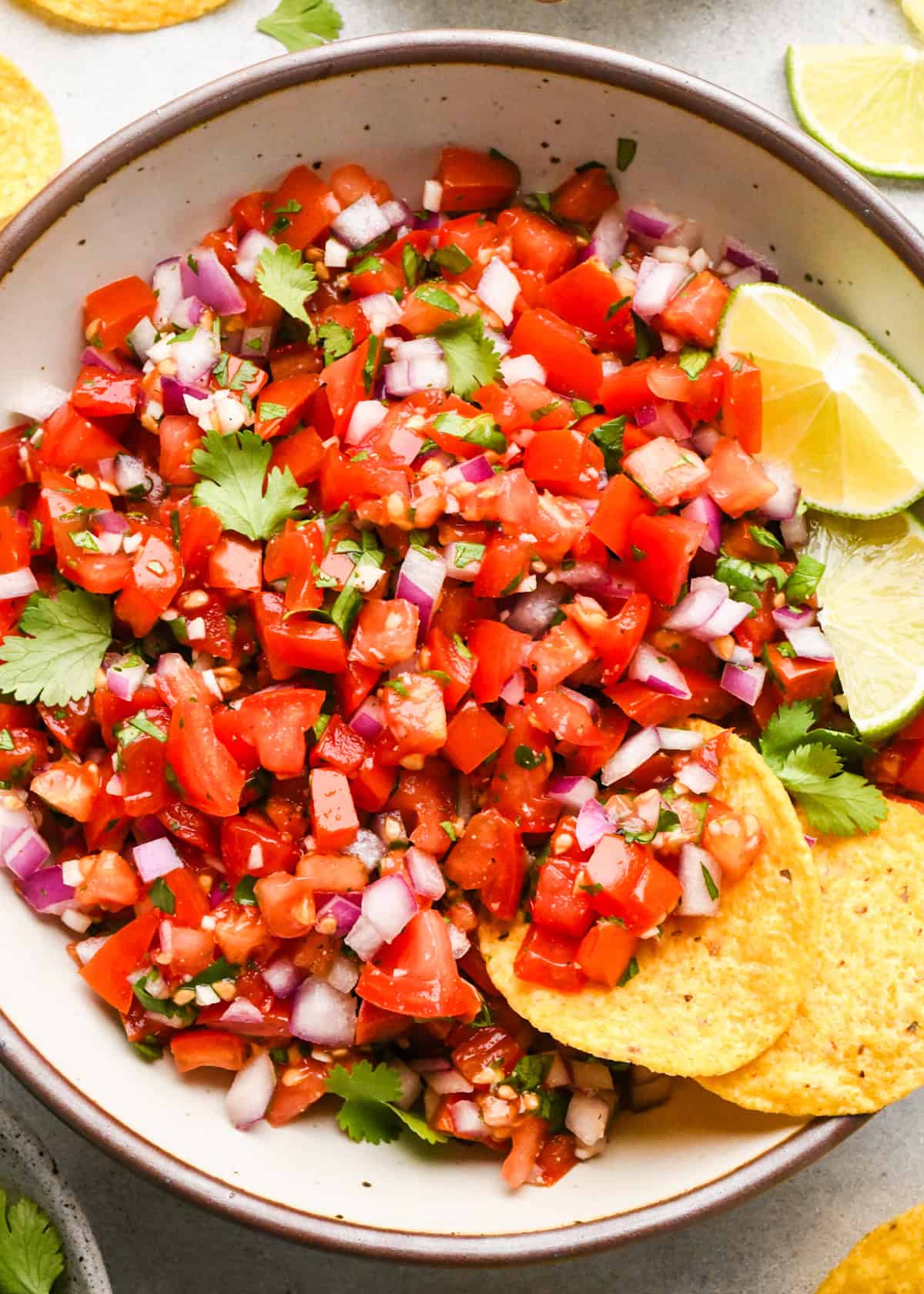 Bowl of homemade pico de gallo made with diced tomatoes, red onion, cilantro, and lime, served with tortilla chips on the side.