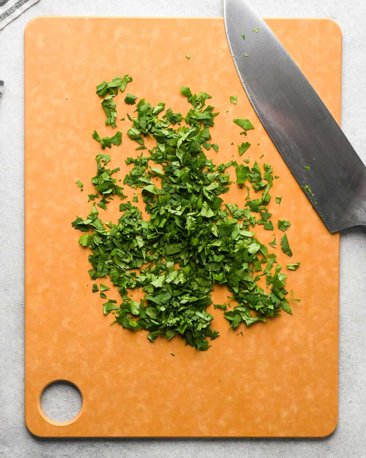 Making pico de Gallo: overhead photo of diced cilantro sitting on a brown cutting board with a knife resting on the board.