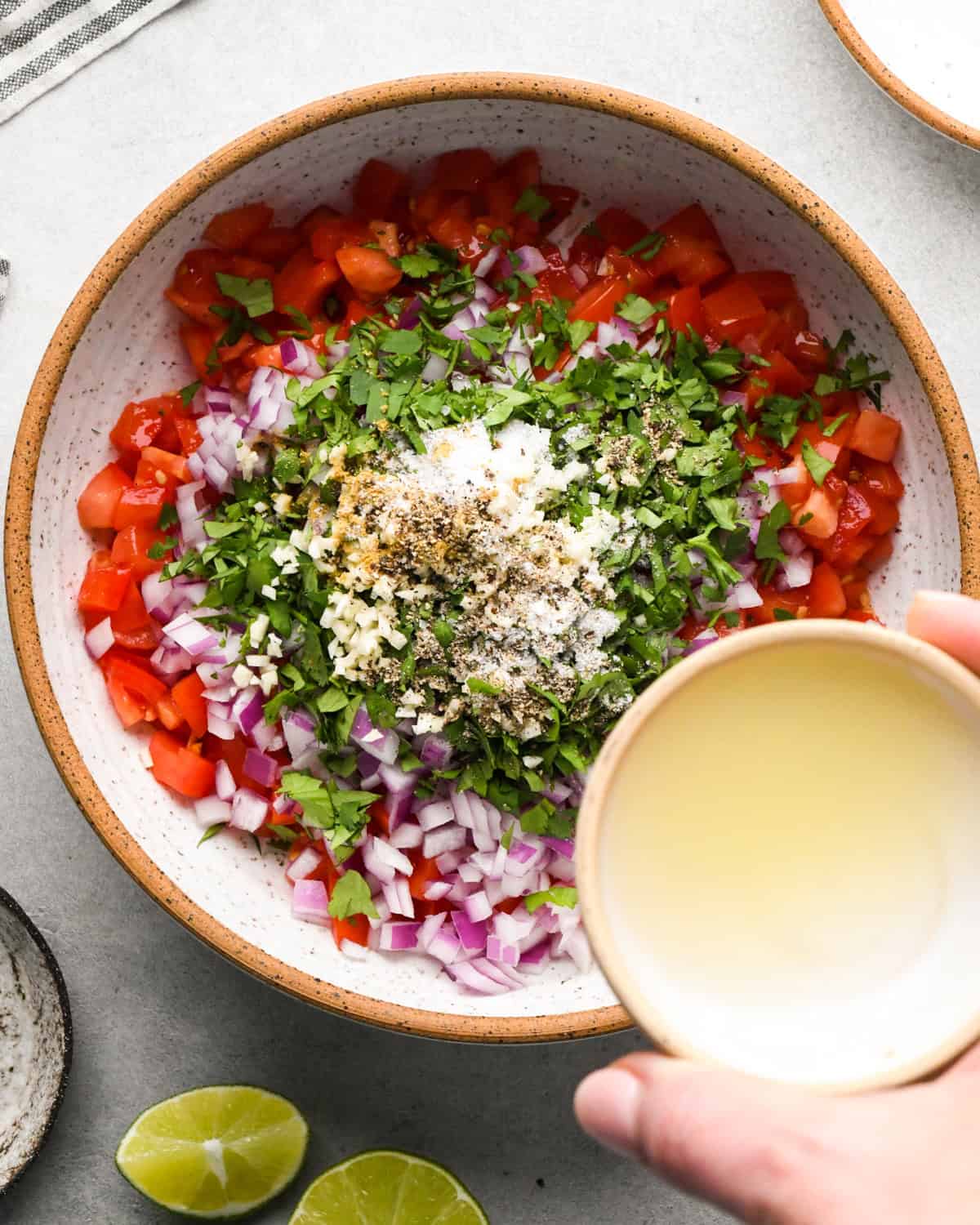 Making pico de Gallo: overhead photo of a hand holding a small bowl of lime juice which is about to be poured into a large bowl with the rest of the ingredients.