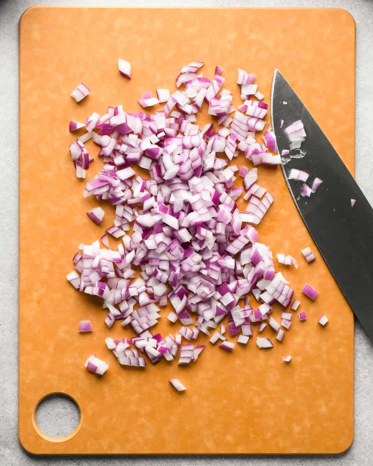 Making pico de Gallo: overhead photo of diced red onion sitting on a brown cutting board with a knife resting on the board.
