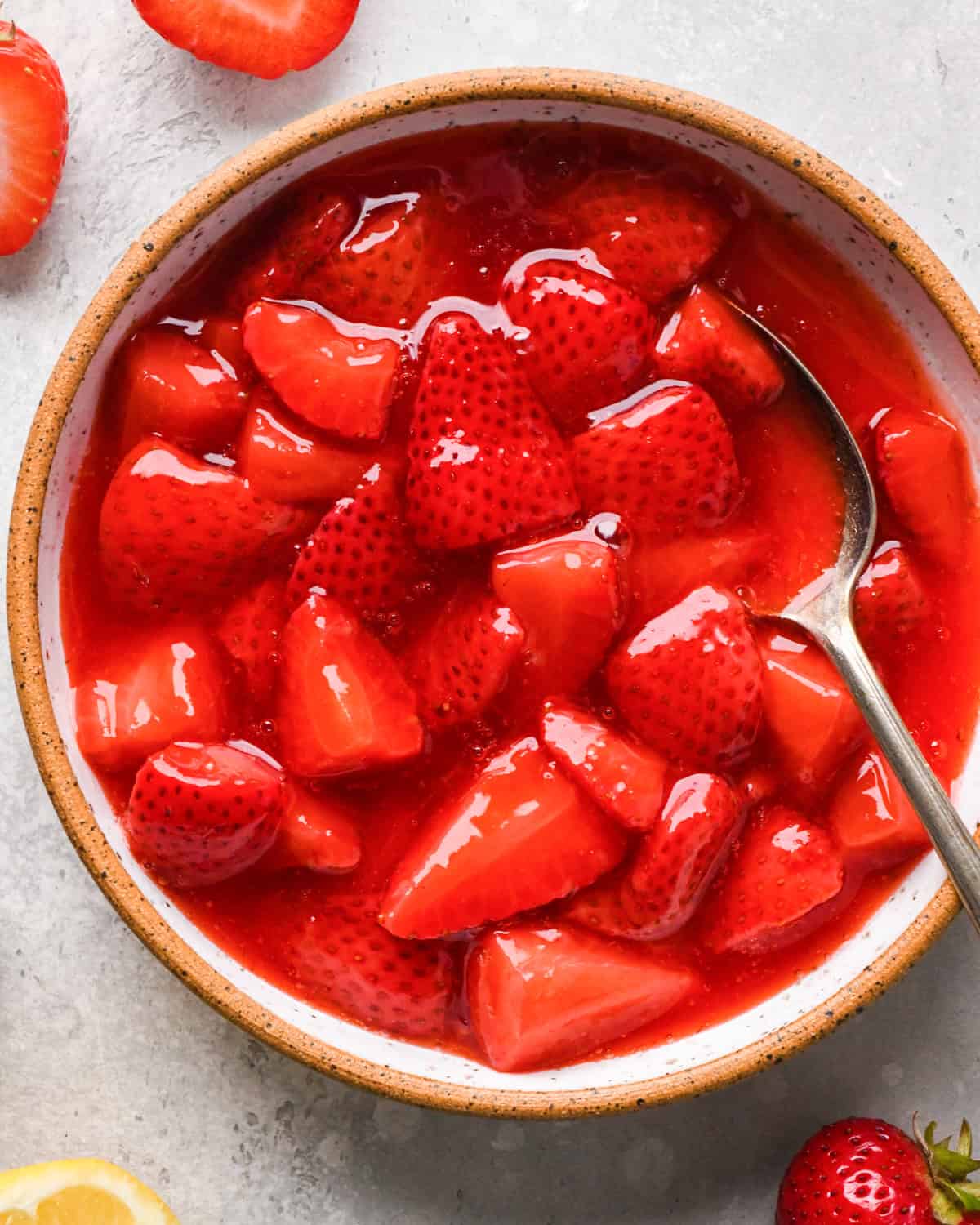 Overhead photo of a white speckled bowl filled with homemade strawberry sauce and being scooped with a spoon.
