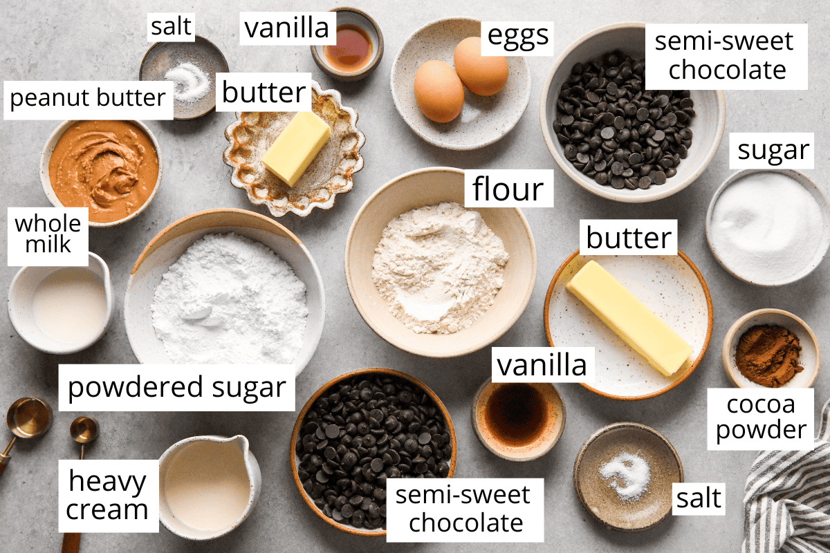 Overhead view of ingredients for buckeye brownies including peanut butter, butter, eggs, flour, cocoa powder, powdered sugar, sugar, vanilla, salt, heavy cream, whole milk, and semi-sweet chocolate chips.