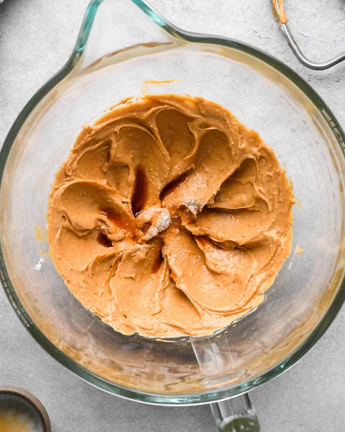 Making buckeye brownies: overhead photo of salt and vanilla added to the beaten butter and peanut butter mixture in a glass measuring bowl.