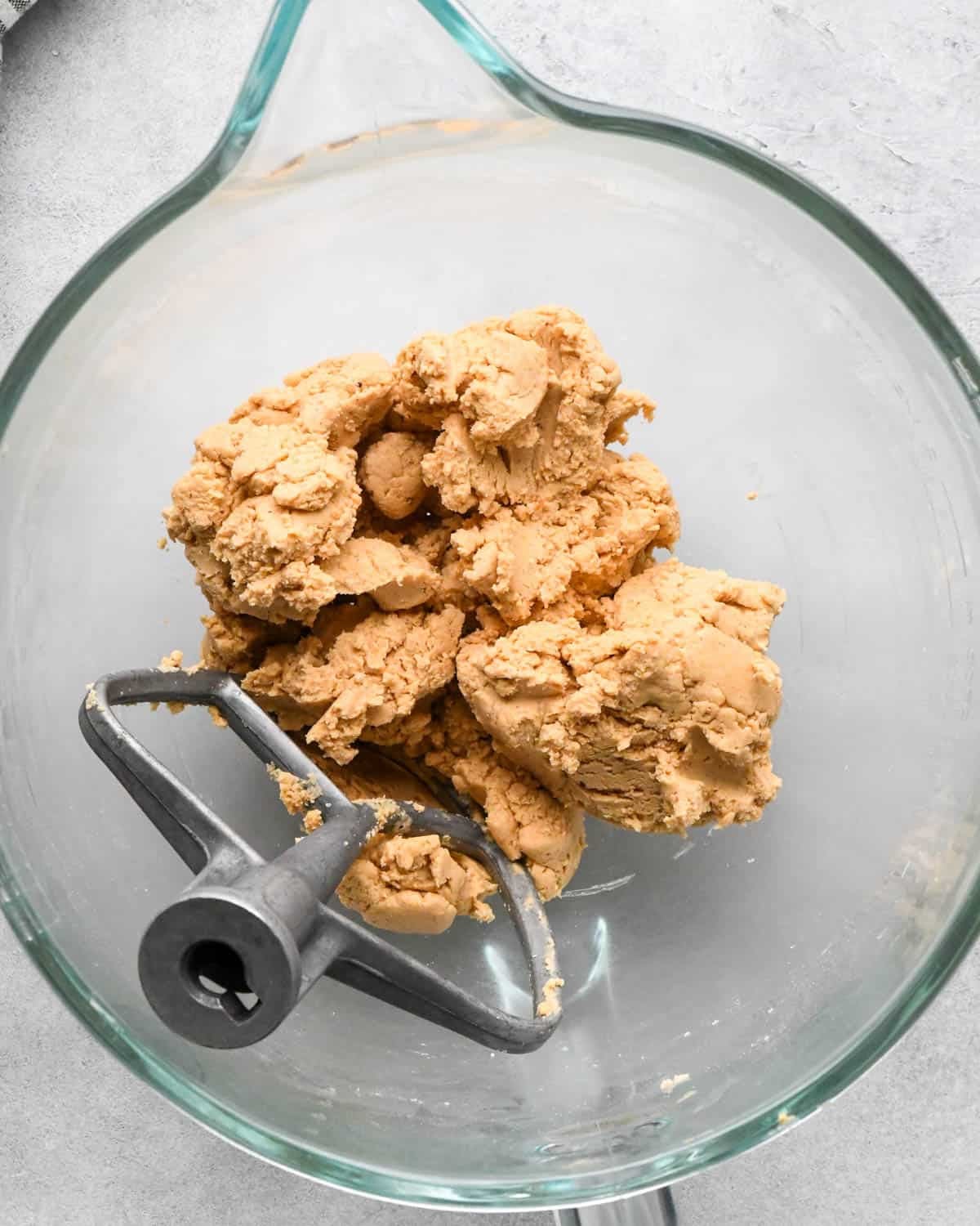 Making buckeye brownies: overhead photo of powdered sugar added to the peanut butter layer mixture and beaten together in a glass measuring bowl. A paddle attachment is resting in the bowl.