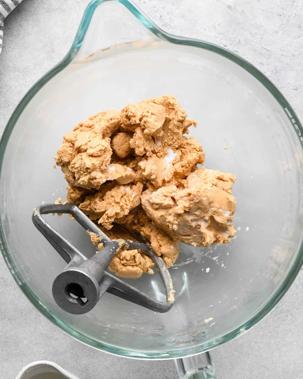 Making buckeye brownies: overhead photo of whole milk added to the peanut butter mixture in a glass measuring bowl. A paddle attachment is resting in the bowl.