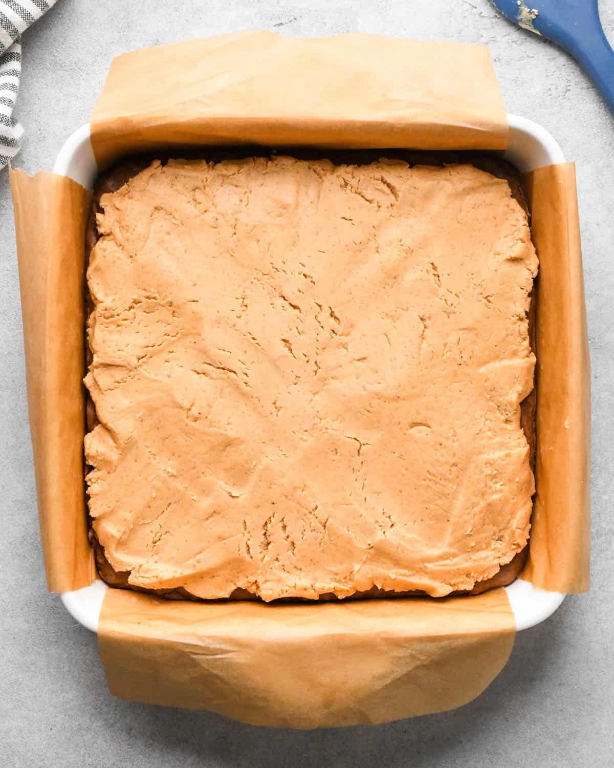 Making buckeye brownies: overhead photo of completed peanut butter mixture poured onto and spread over the chilled brownie layer in a 9x9" baking dish.