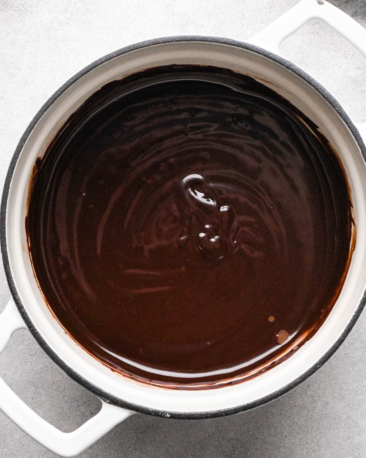 Making chocolate ganache: overhead photo of heavy cream and chocolate melted and whisked together in a large white pot.