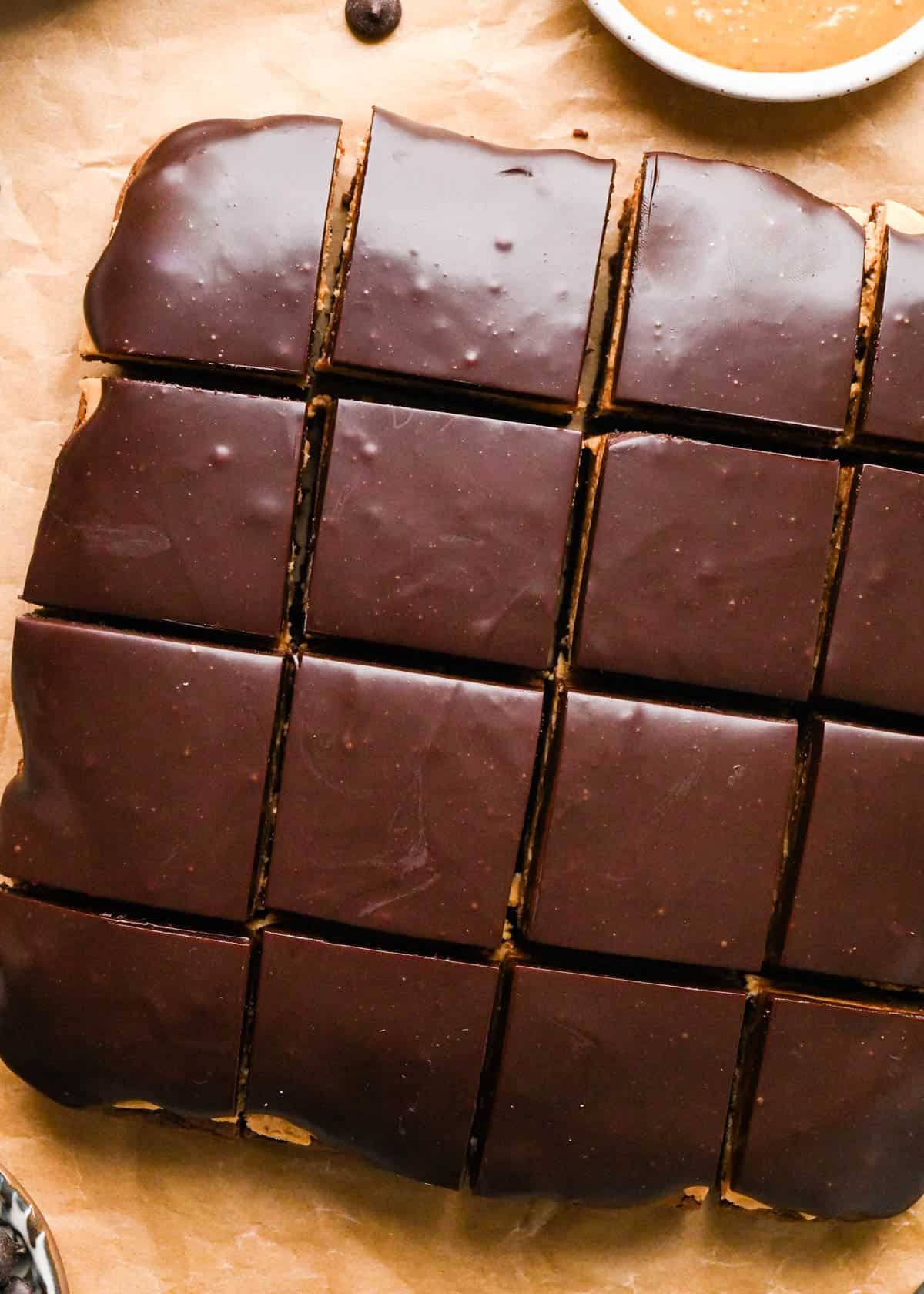 Making buckeye brownies: overhead photo of completed buckeye brownies - with a brownie layer, a peanut butter layer, and a chocolate ganache layer - cut into 16 squares on a large sheet of parchment paper.