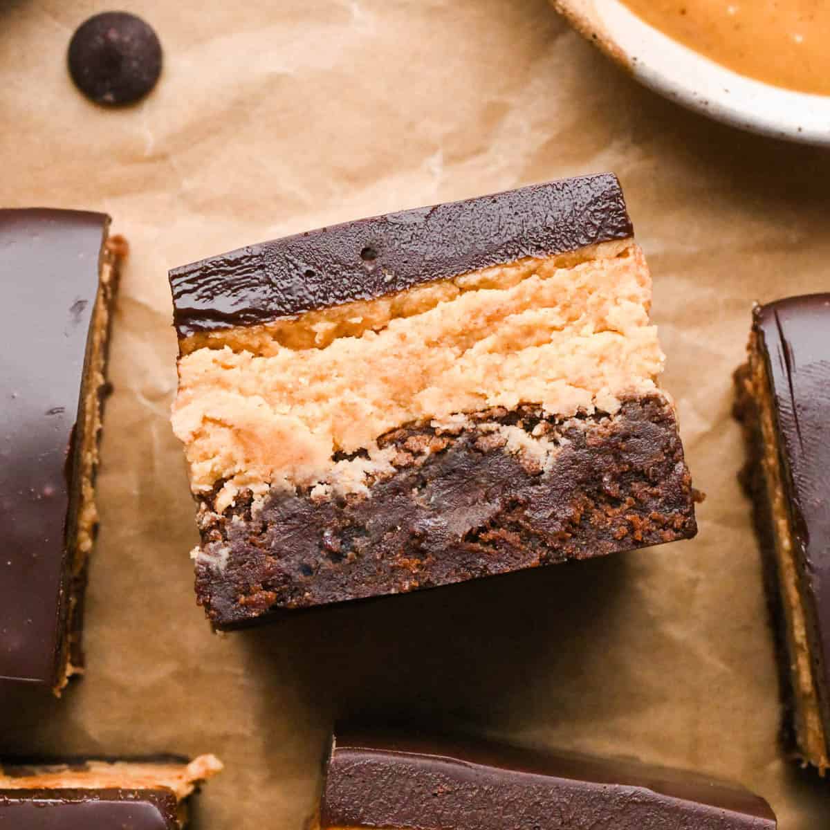 Overhead photo of buckeye brownies with a fudgy chocolate brownie base, creamy peanut butter layer, and smooth chocolate ganache topping on a sheet of parchment paper.