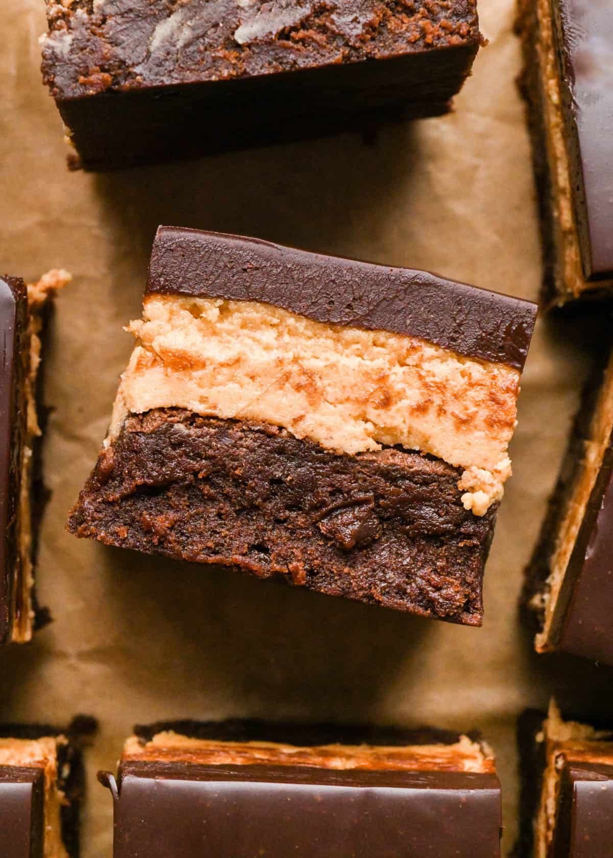 Overhead photo of buckeye brownies with a fudgy chocolate brownie base, creamy peanut butter layer, and smooth chocolate ganache topping on a sheet of parchment paper.