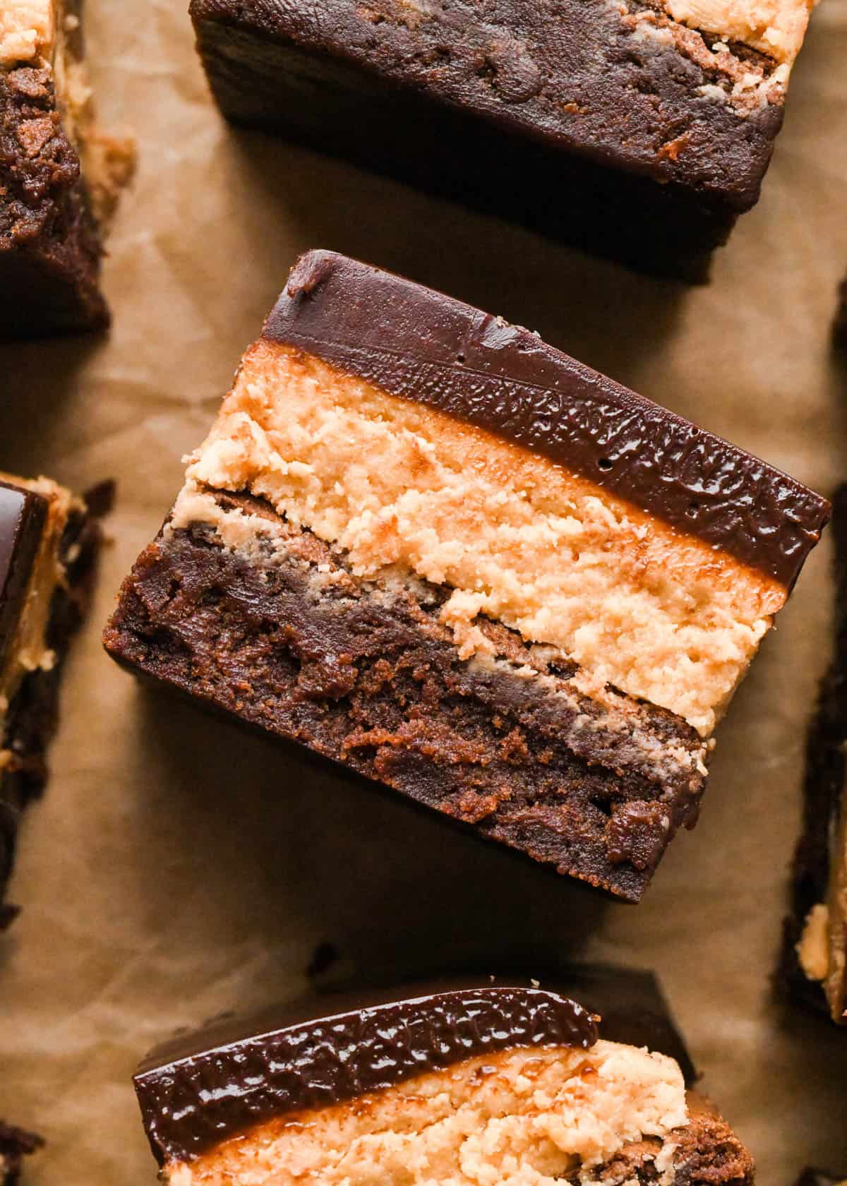 Overhead photo of buckeye brownies with a fudgy chocolate brownie base, creamy peanut butter layer, and smooth chocolate ganache topping on a sheet of parchment paper.