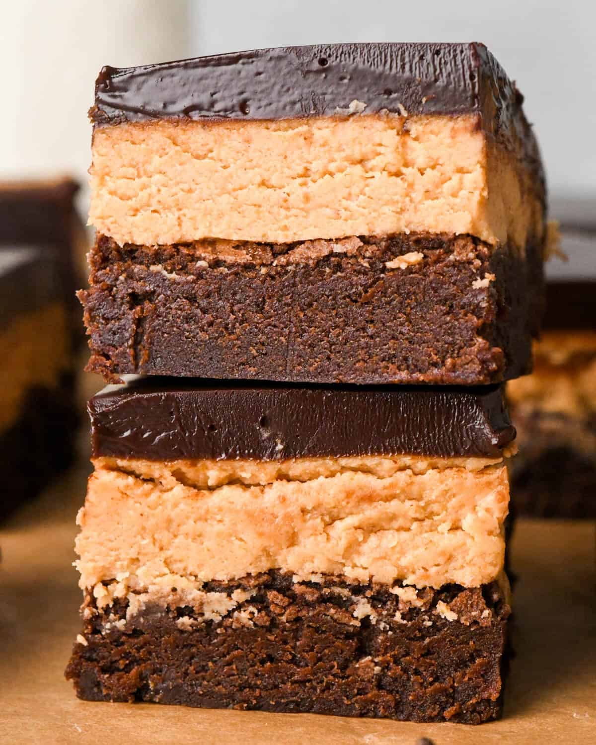 Up-close photo of stacked buckeye brownies with a fudgy chocolate brownie base, creamy peanut butter layer, and smooth chocolate ganache topping on a wooden surface.