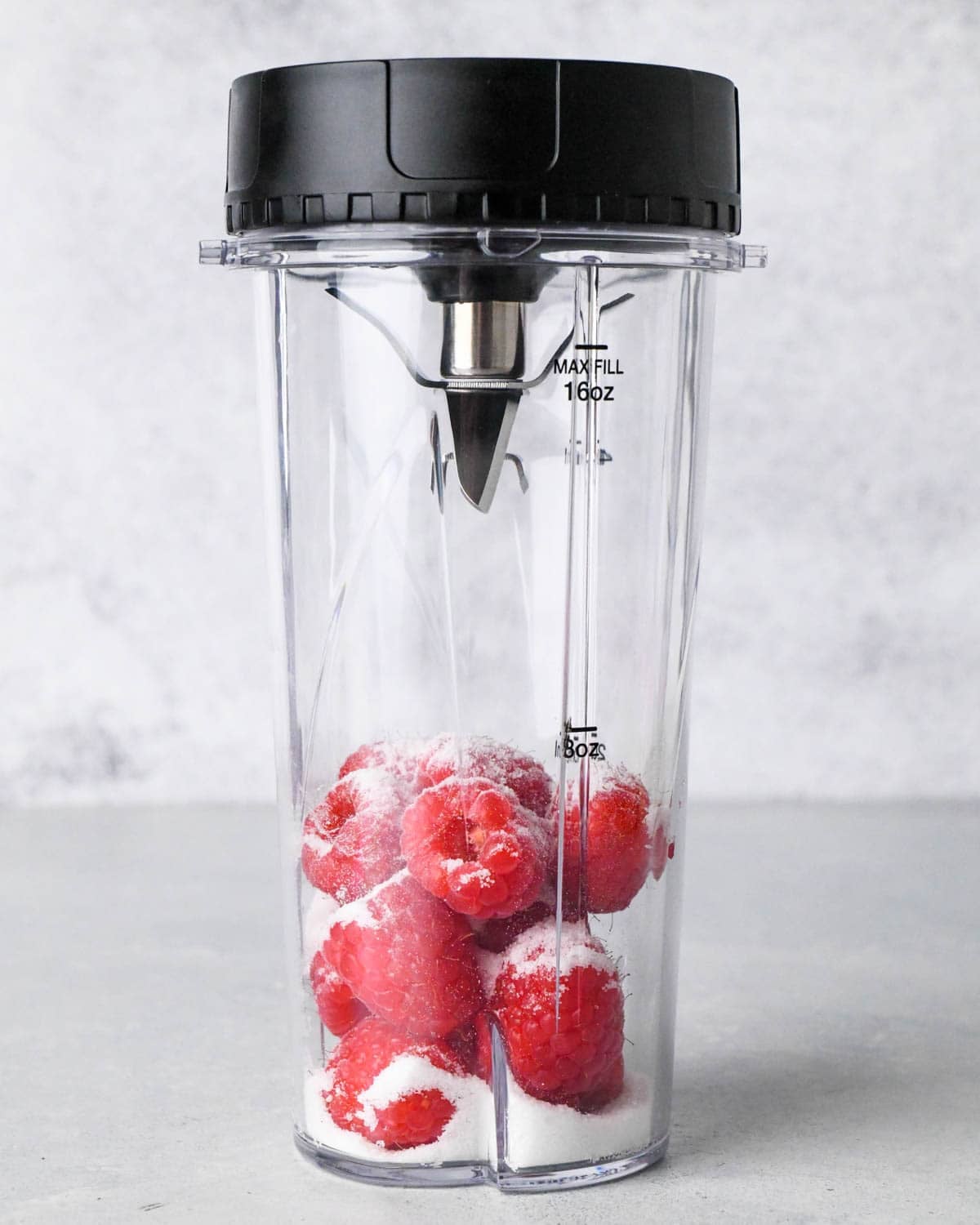 how to make raspberry frosting - front view of raspberries and sugar in a small blending container before blending