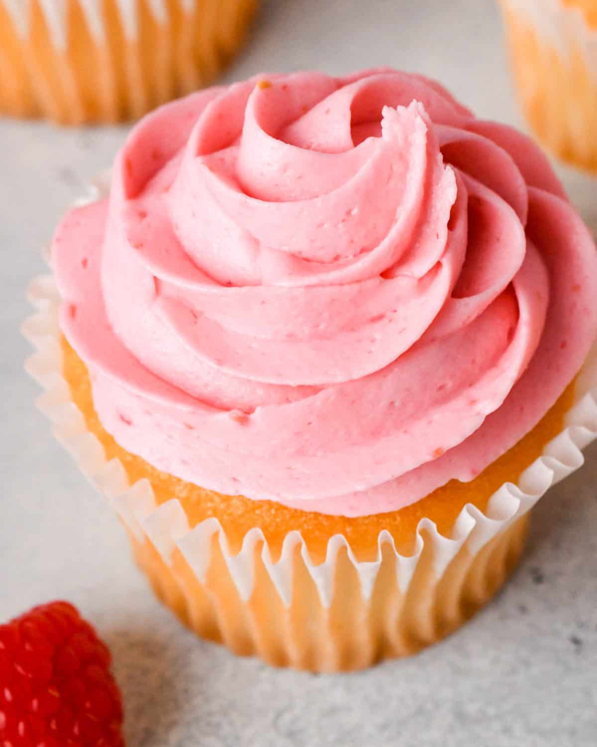 overhead view of raspberry frosting on top of a vanilla cupcake in a wrapper with a fresh raspberry on top