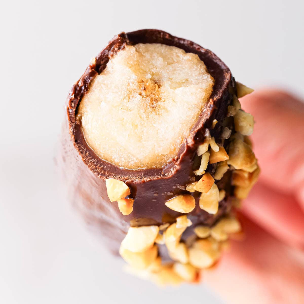 Up-close photo of a chocolate dipped and peanut-coated frozen banana with a bite taken out of it to show the inside.