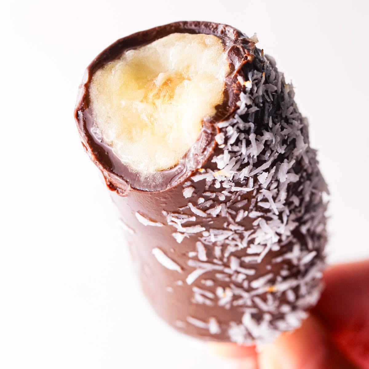 Up-close photo of a chocolate dipped and coconut-coated frozen banana with a bite taken out of it to show the inside.