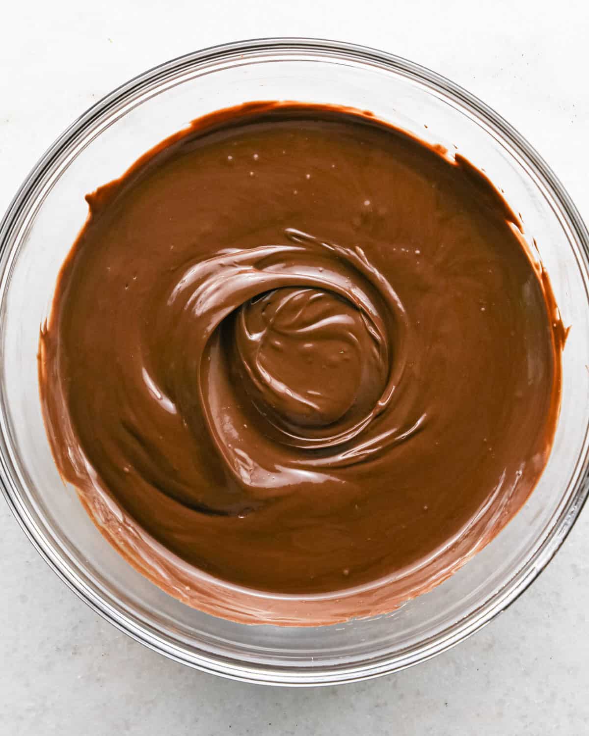 Making chocolate dipped frozen bananas: overhead photo of a clear glass bowl with melted chocolate candy melts.