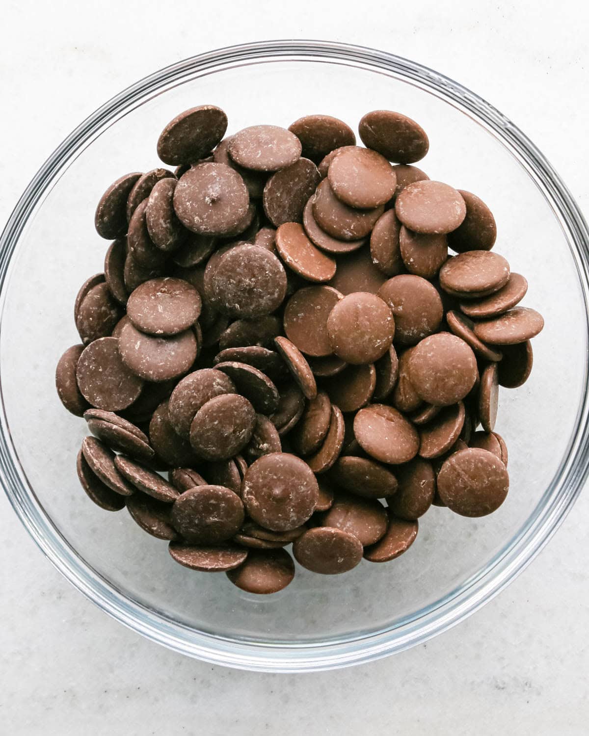 Making chocolate dipped frozen bananas: overhead photo of a clear glass bowl filled with chocolate candy melts.