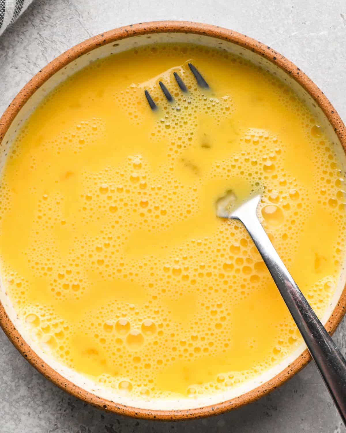 Making Pad Thai: overhead photo of an egg cracked and beaten in a small bowl with a fork.