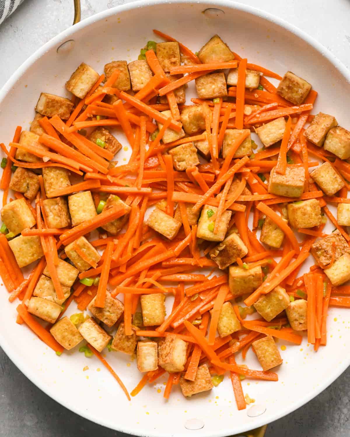 Making Pad Thai: overhead photo of cooked tofu, carrots, onion, garlic, and oil together in a skillet. The carrots appear done (soft).