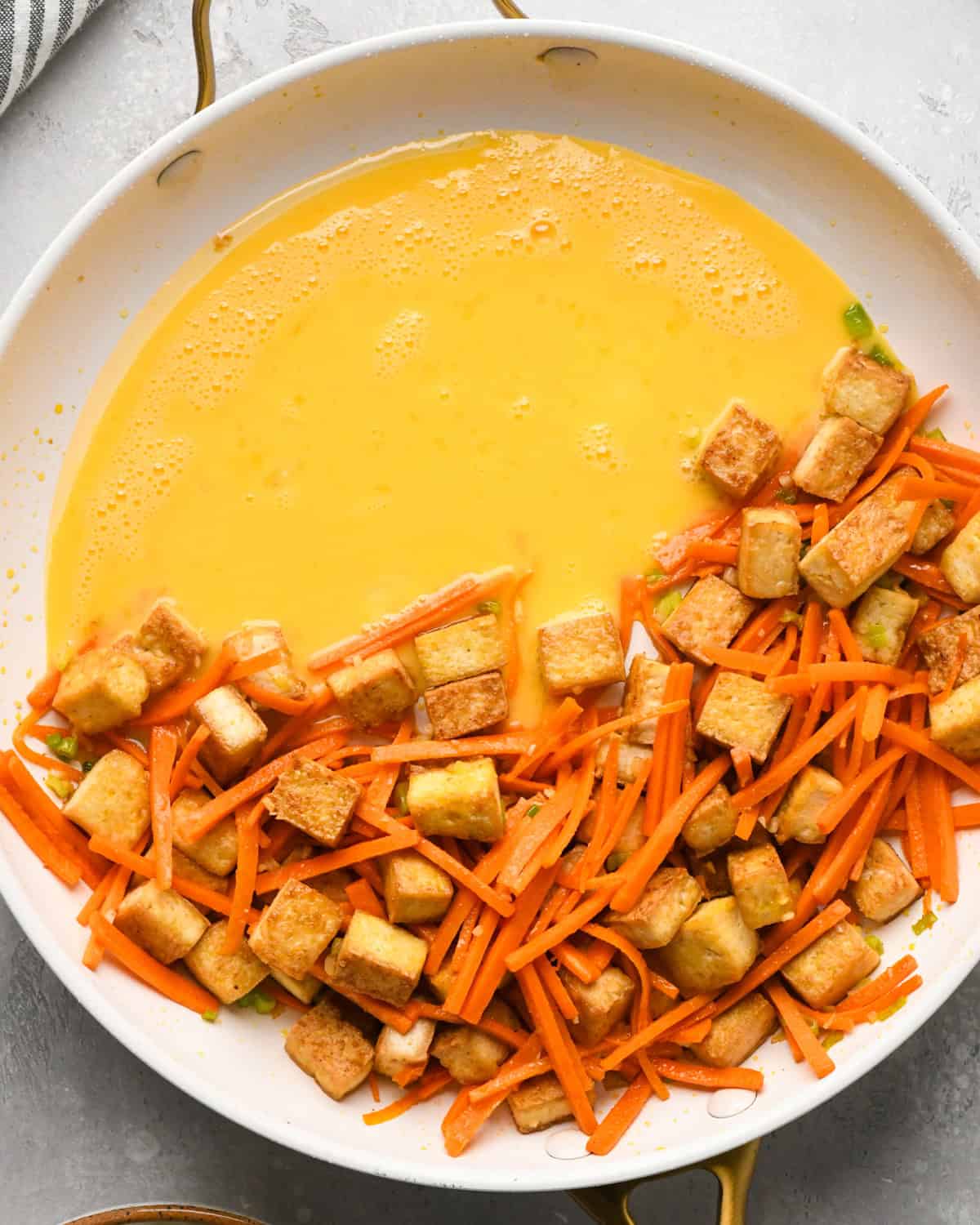 Making Pad Thai: overhead photo of tofu, carrots, onion, and garlic added to beaten egg mixture in a skillet.