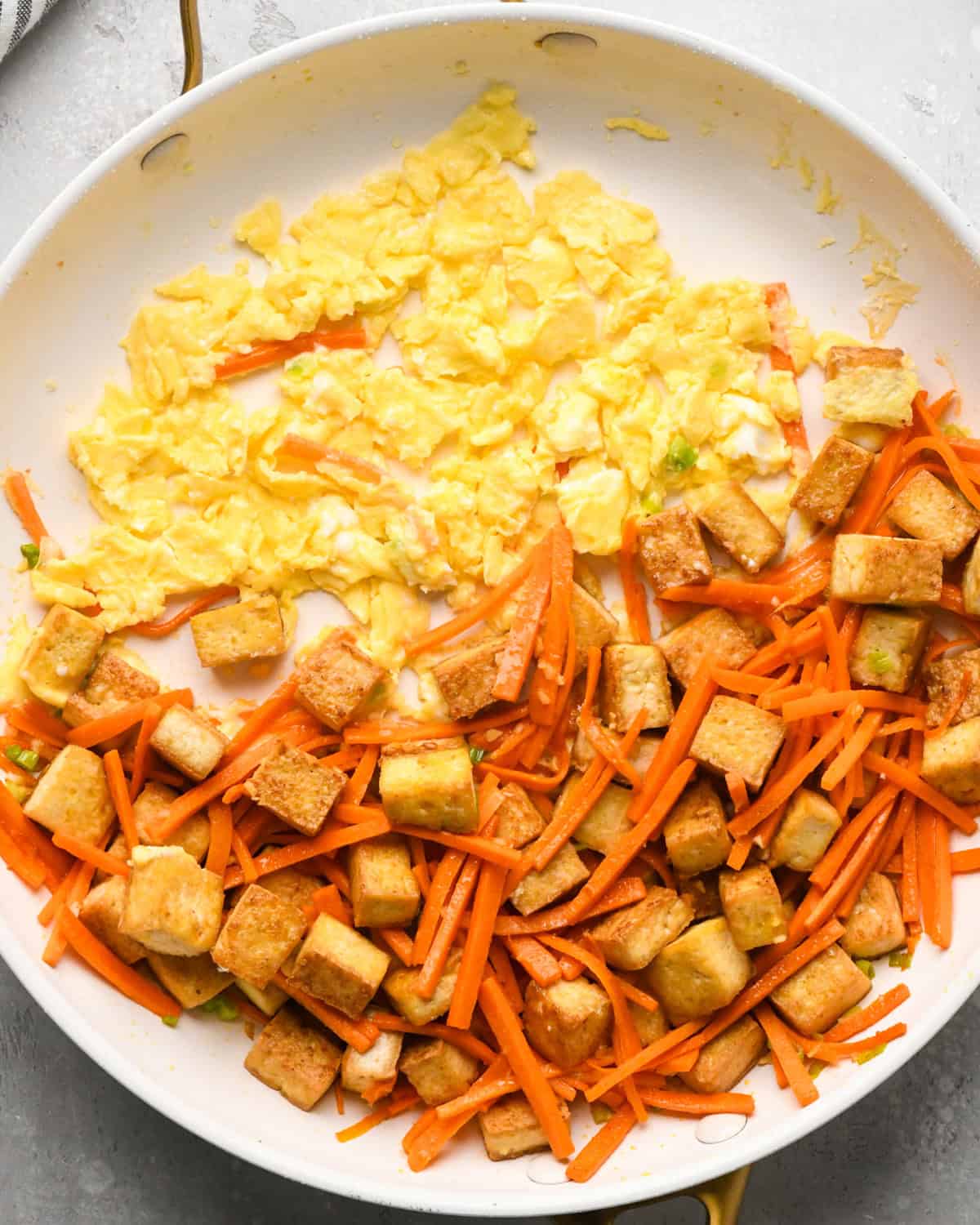 Making Pad Thai: overhead photo of an egg scrambled in a skillet with cooked tofu, carrots, onion, and garlic.