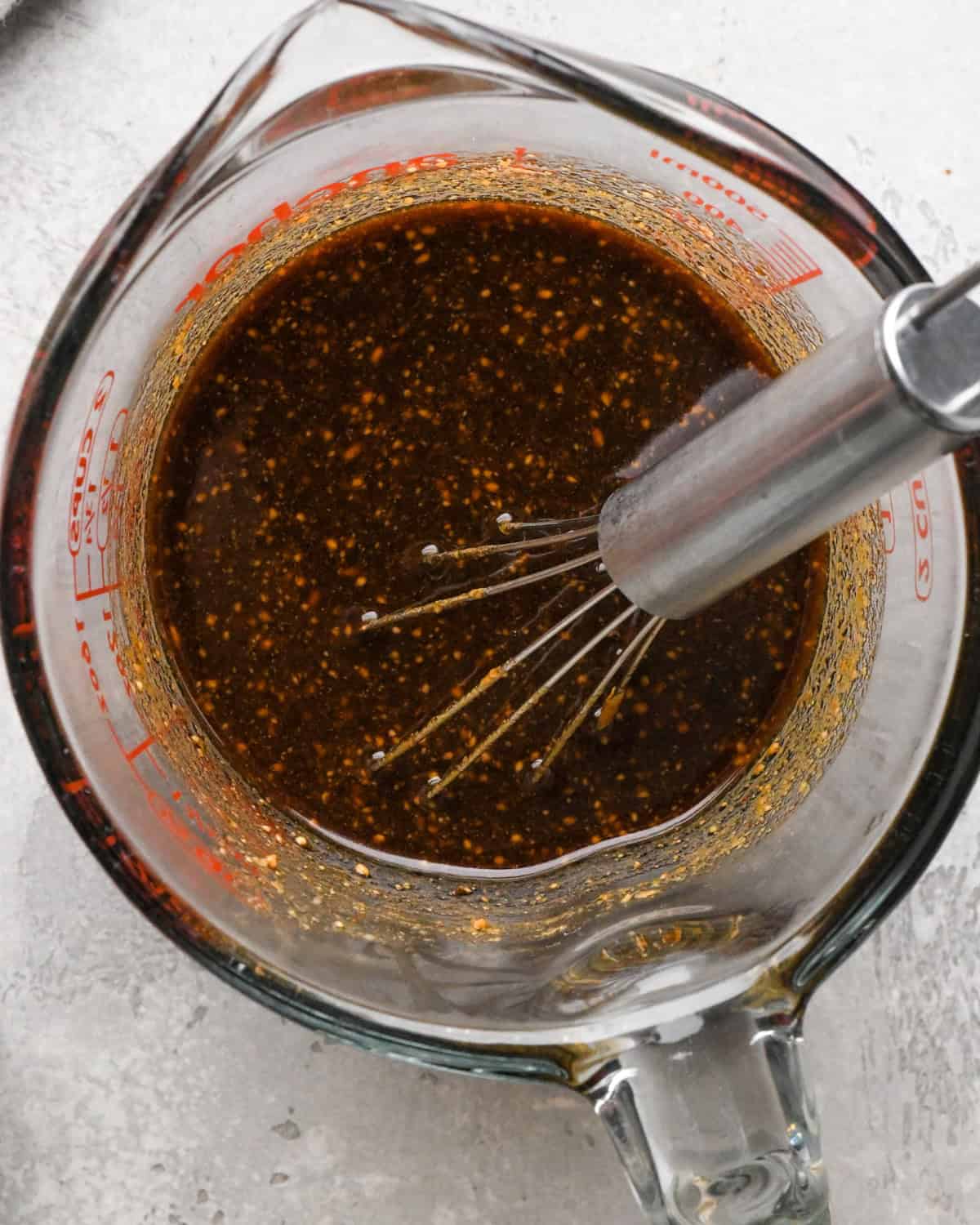 Overhead photo of soy sauce, water, brown sugar, tamarind paste, lime juice, chili sauce and peanut butter shown in a measuring cup and whisked together.