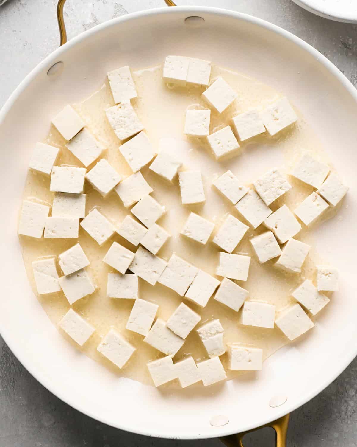 Making Pad Thai: overhead photo of tofu cooking in oil in a large white skillet.