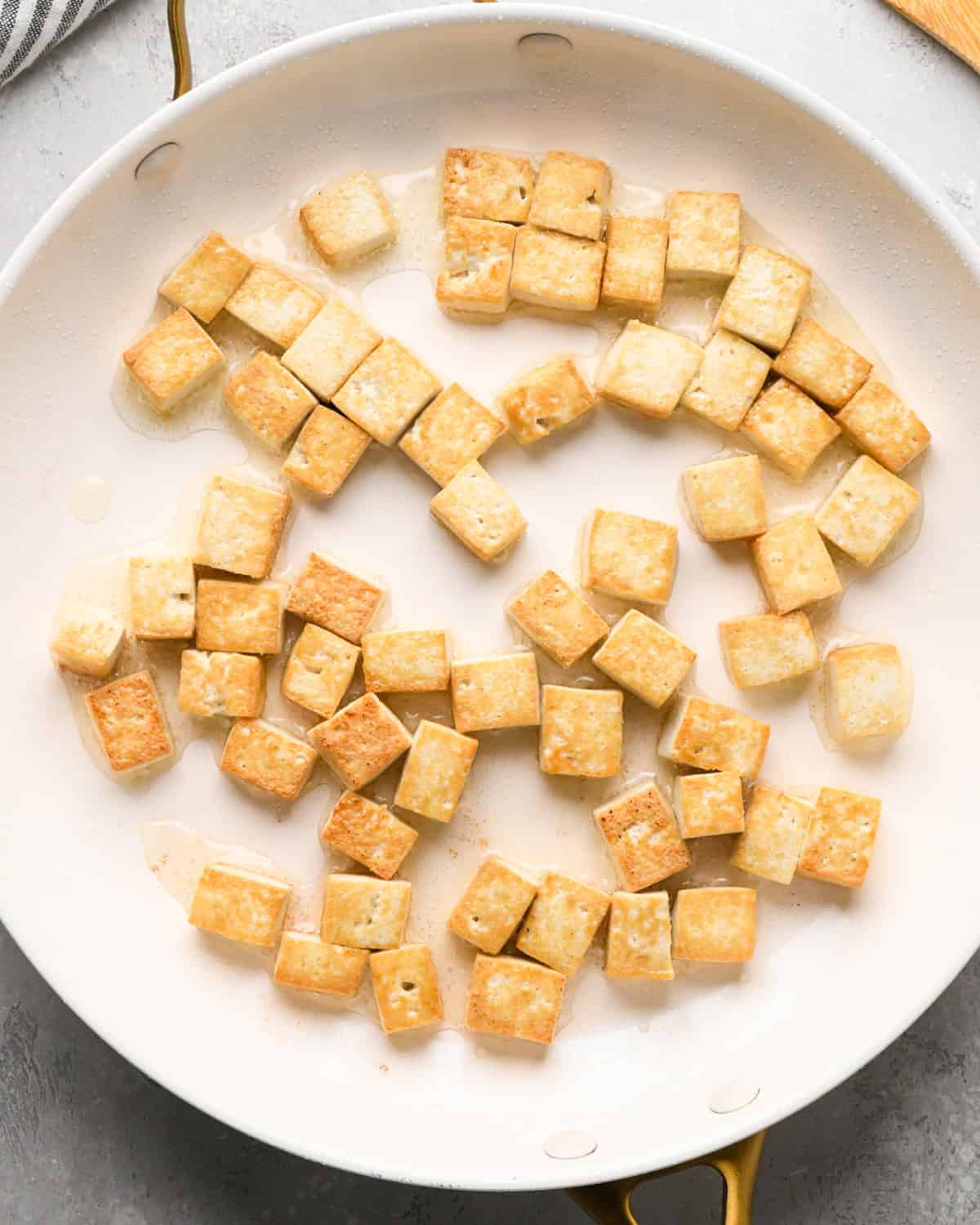 Making Pad Thai: overhead photo of tofu cooking in oil in a large white skillet. The tofu is lightly browned to show doneness.