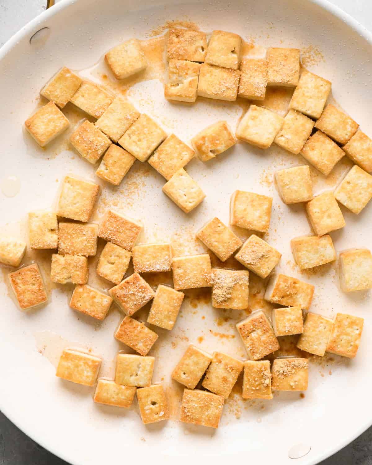Making Pad Thai: overhead photo of tofu cooking in oil in a large white skillet. The tofu is lightly browned to show doneness.