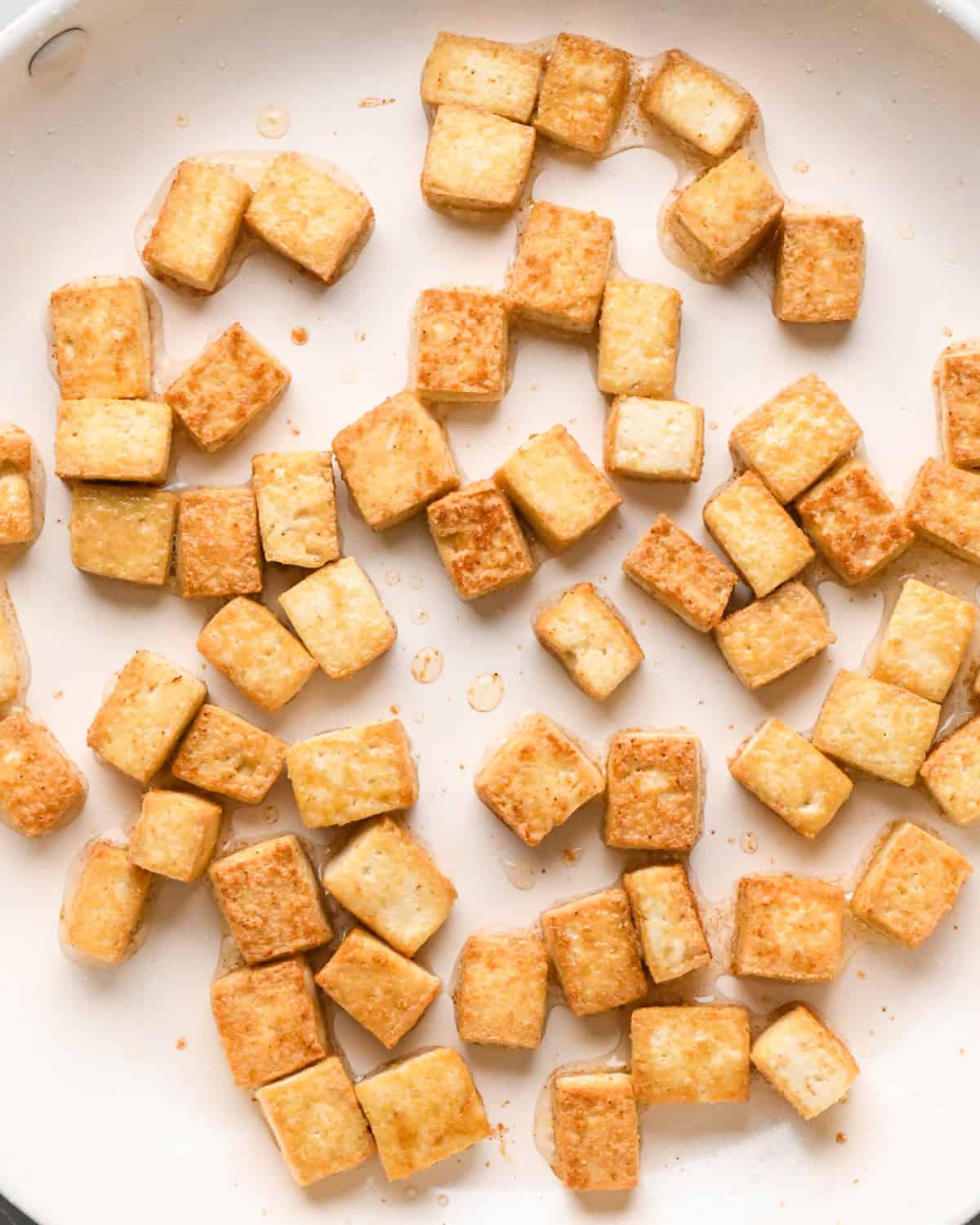 Making Pad Thai: overhead photo of tofu cooking in oil in a large white skillet. The tofu is lightly browned to show doneness.