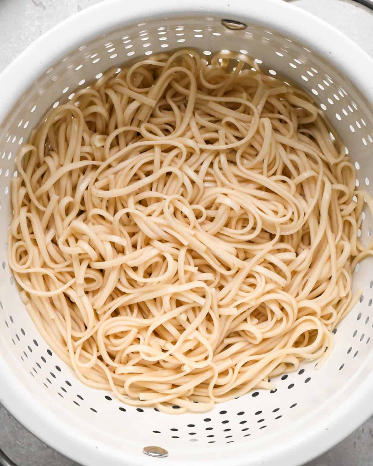 Making Pad Thai: overhead photo of cooked pasta noodles shown drained in a large white colander.