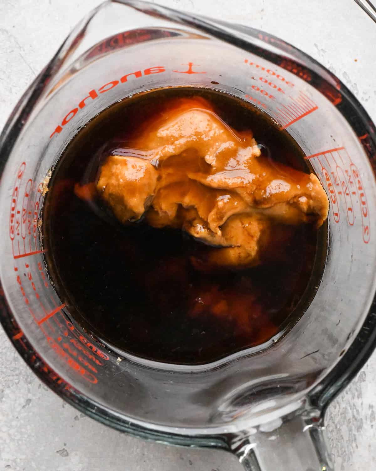 Overhead photo of soy sauce, water, brown sugar, tamarind paste, lime juice, chili sauce and peanut butter shown in a measuring cup.