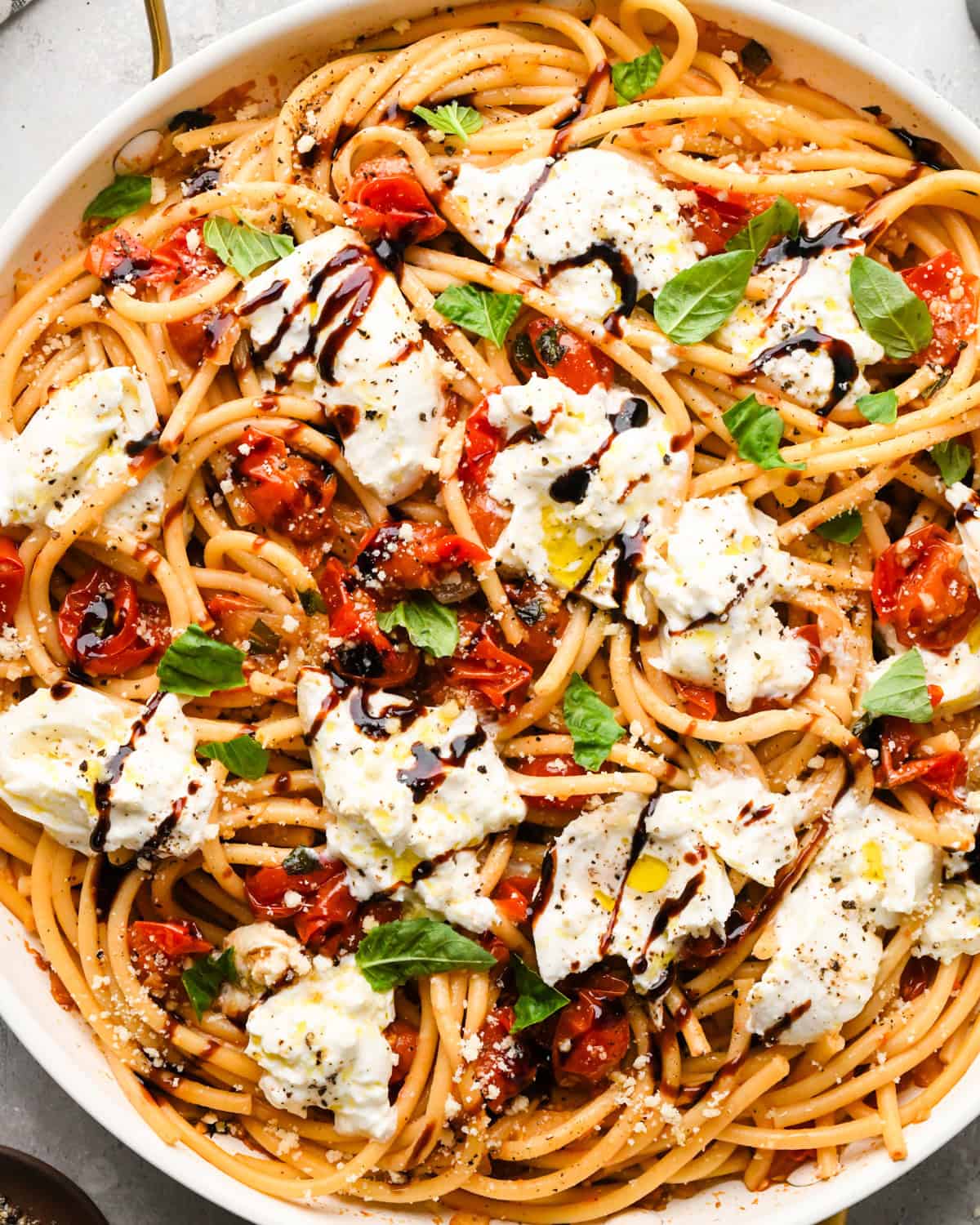 Making pasta with burrata cheese: overhead photo of balsamic vinegar drizzled on top of the pasta, sautéed tomato mixture, and burrata cheese in a skillet. Ready to serve.