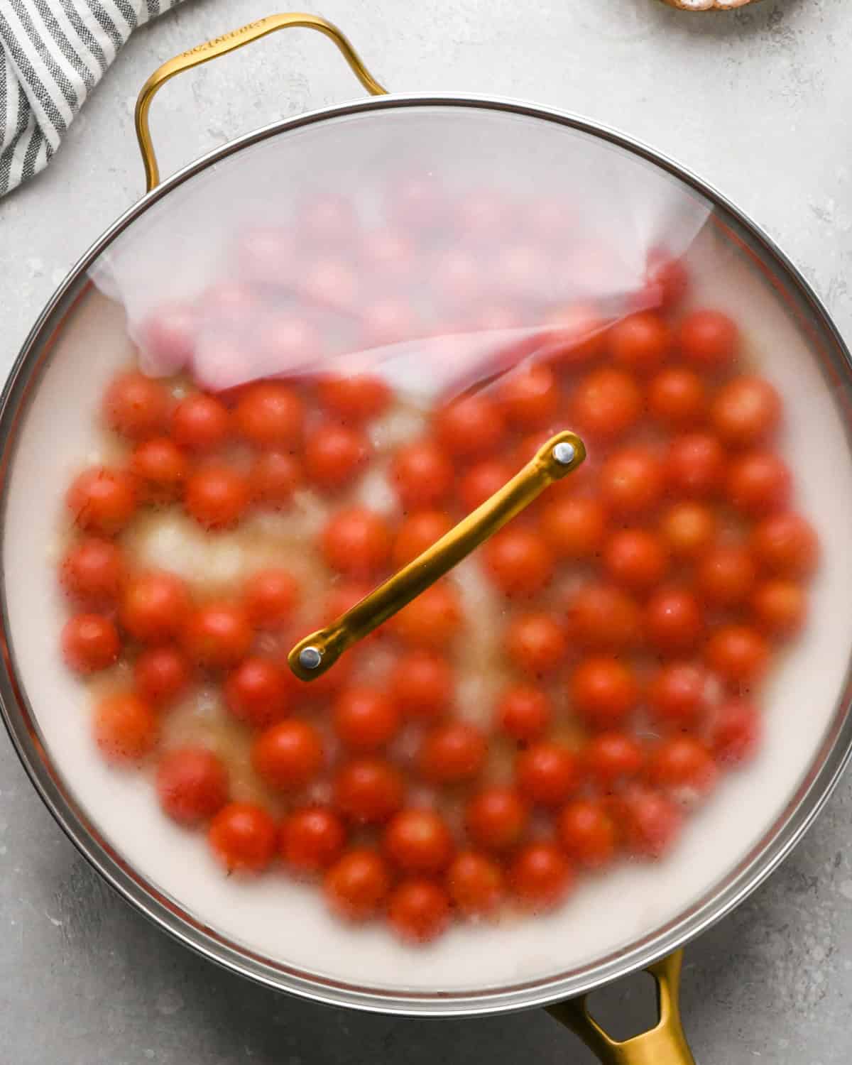 Making pasta with burrata cheese: overhead photo of tomatoes, garlic, and onions shown in a large gold and white skillet and covered with a lid.
