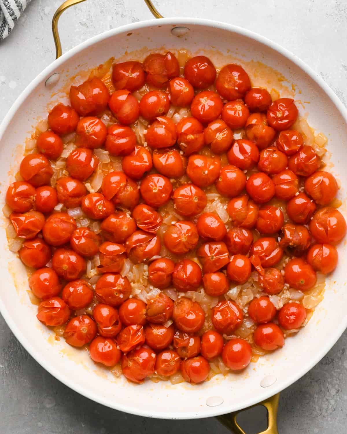Making pasta with burrata cheese: overhead photo of tomatoes, garlic, and onions sautéed together in a large skillet.