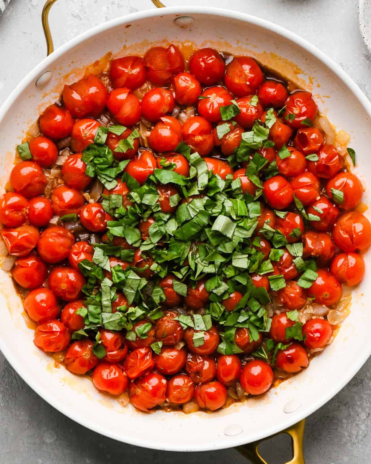 Making pasta with burrata cheese: overhead photo of chopped basil being added to a skillet with sautéed tomatoes, garlic, and onion.